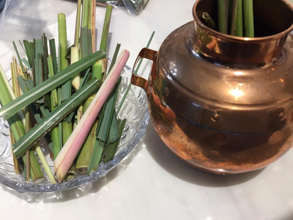 Fresh lemongrass beside a traditional copper steam distillation vessel