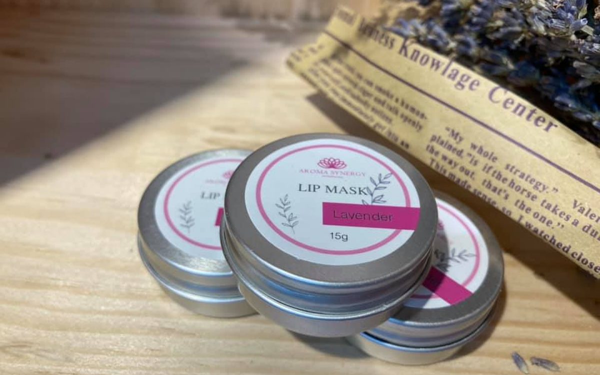 Lavender lip mask tins on a sunlit wooden table with a sprig of dried lavender